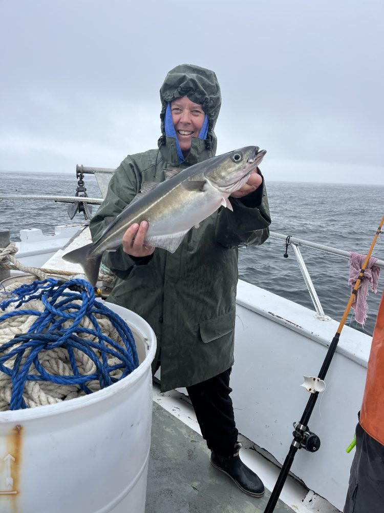 Person in raincoat holding a fish on a boat with ropes.