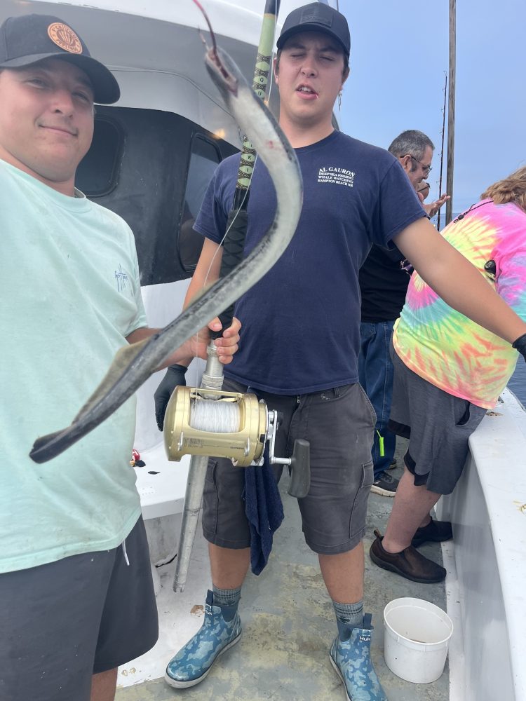 Two people on a boat holding a curved fish with a fishing reel.