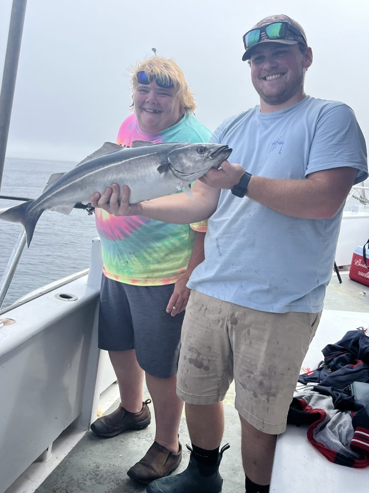 Two people smiling on a boat, holding a large fish between them.