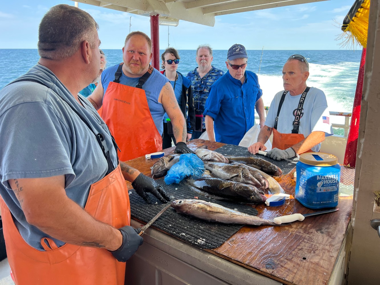 Men on a boat discuss caught fish on a table by the ocean.