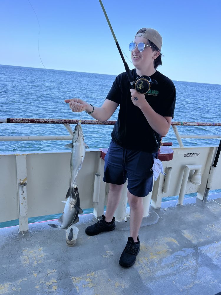 Person on boat holding fishing rod with caught fish, ocean in background.