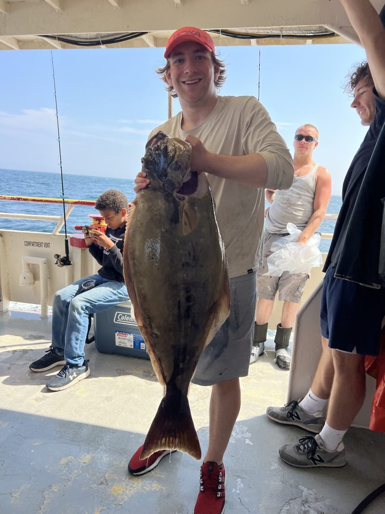 Person in red cap holding a large fish on a boat with others in the background.