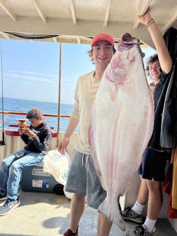Person holding large fish on boat, with ocean view in background.