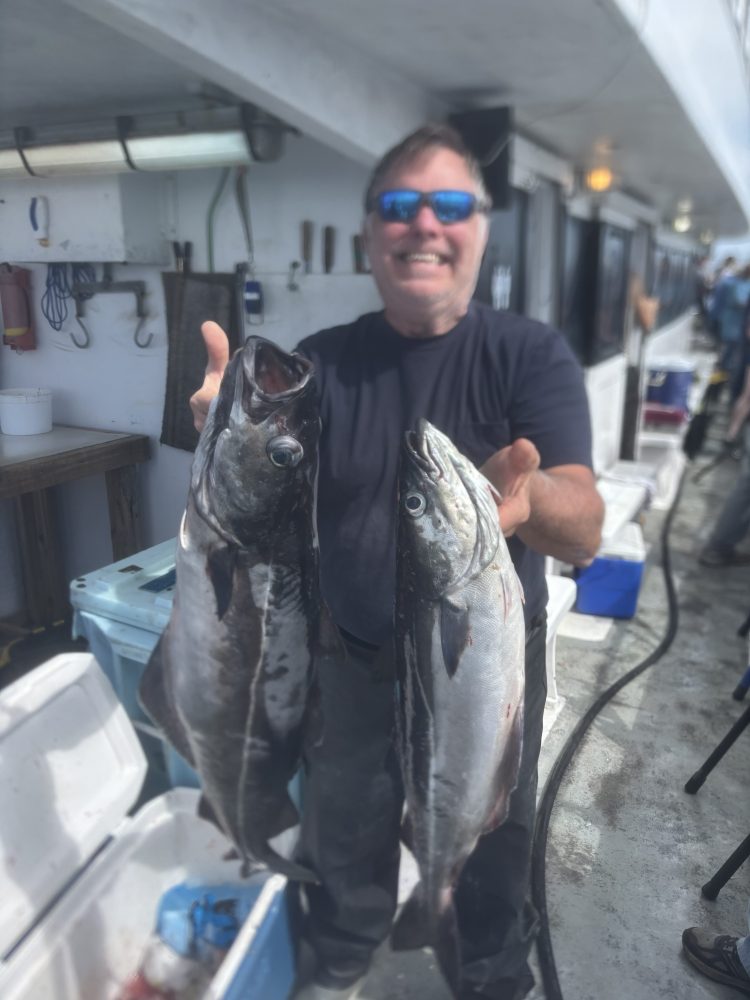 Person on a boat holding two large fish, smiling with blurred background.