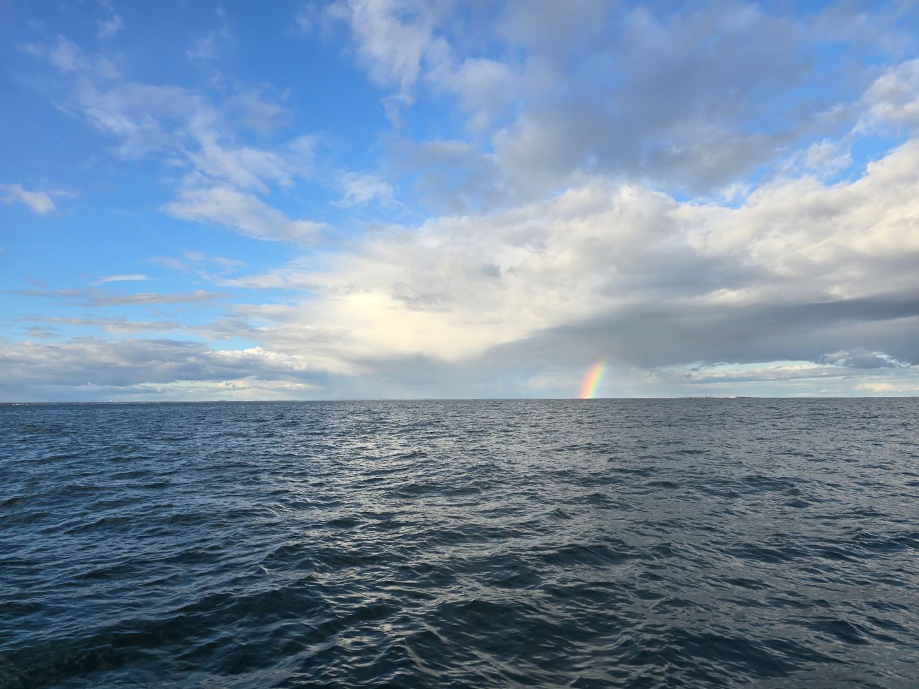Ocean under cloudy sky with a rainbow near the horizon.