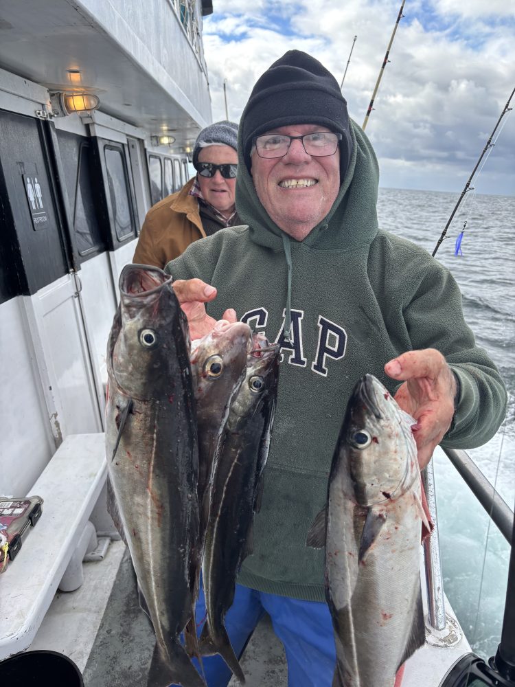 Smiling man holding four fish on a boat with another person in the background.