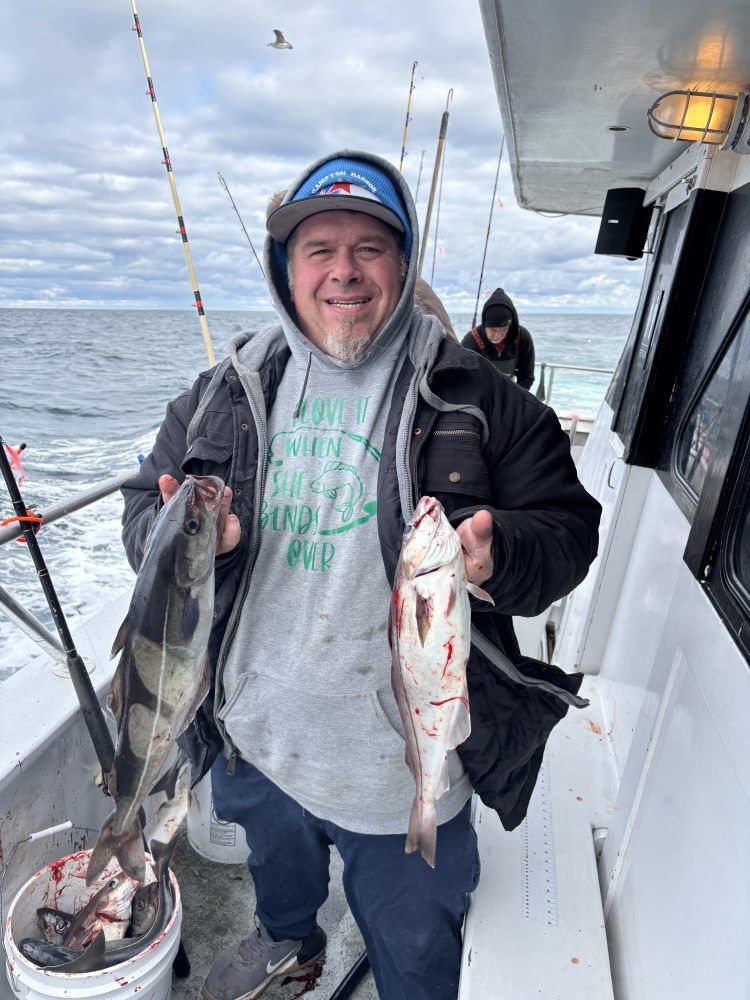 Smiling person on a boat holding two fish with a cloudy ocean backdrop.