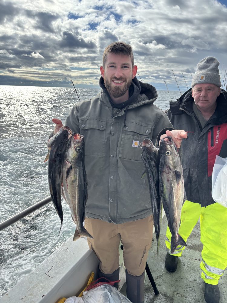 Person on a boat holding multiple fish with another person standing beside.