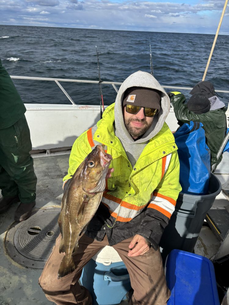 Person in bright jacket holding fish on a boat with ocean background.