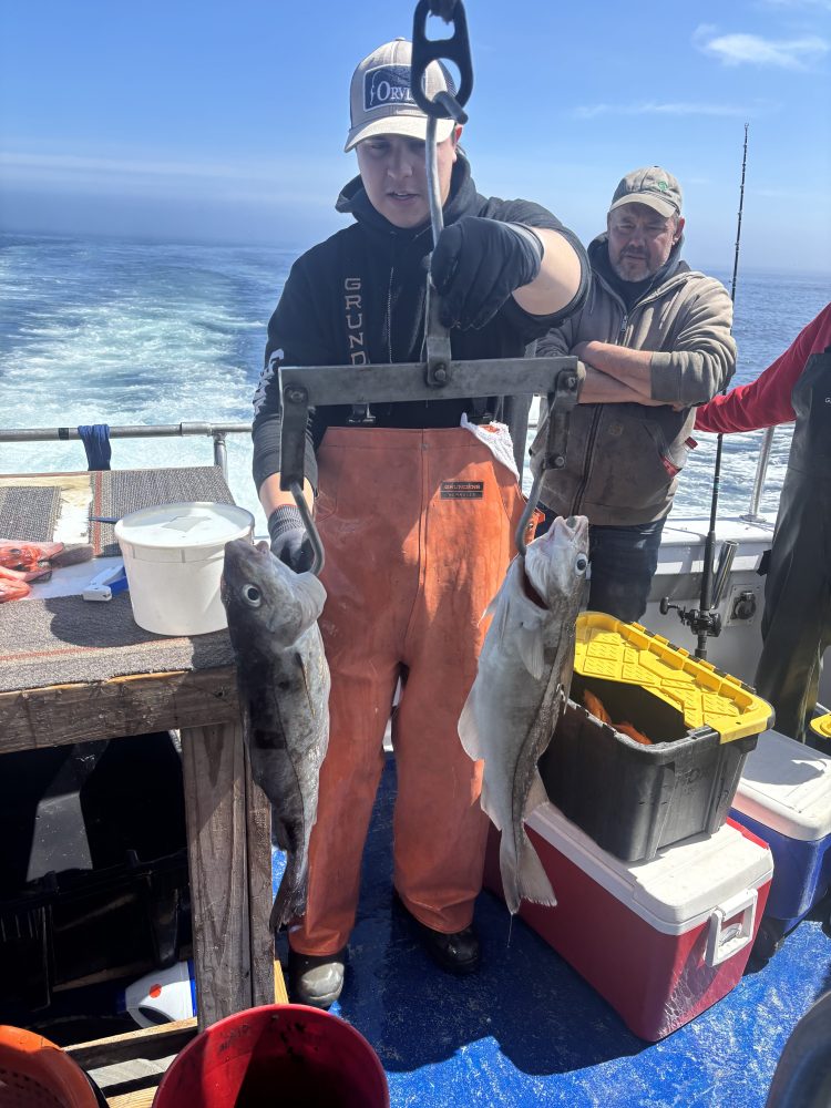 Two people on a boat holding large fish with ocean background.