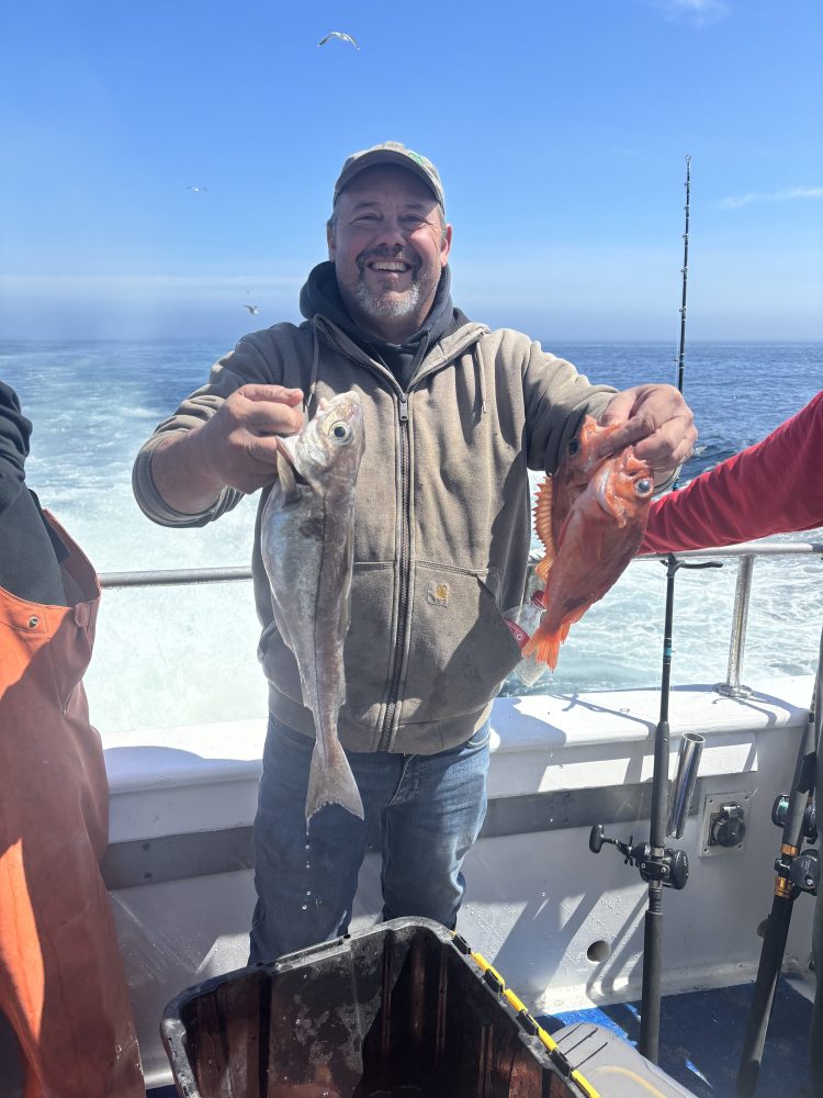 Man on boat holding two fish, ocean in background.