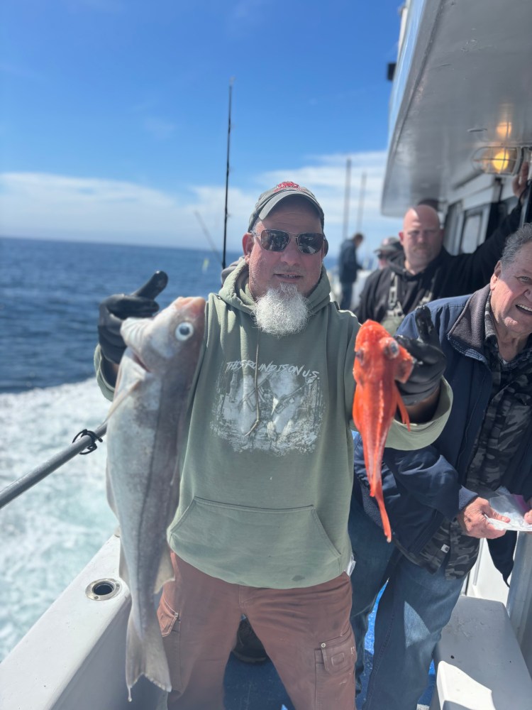 Man on boat holding two fish with ocean in background.
