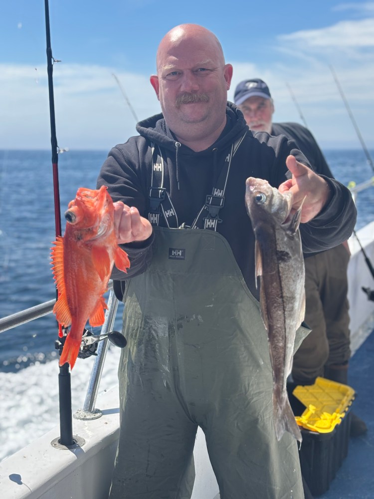 Man holding two fish on a boat with ocean background.