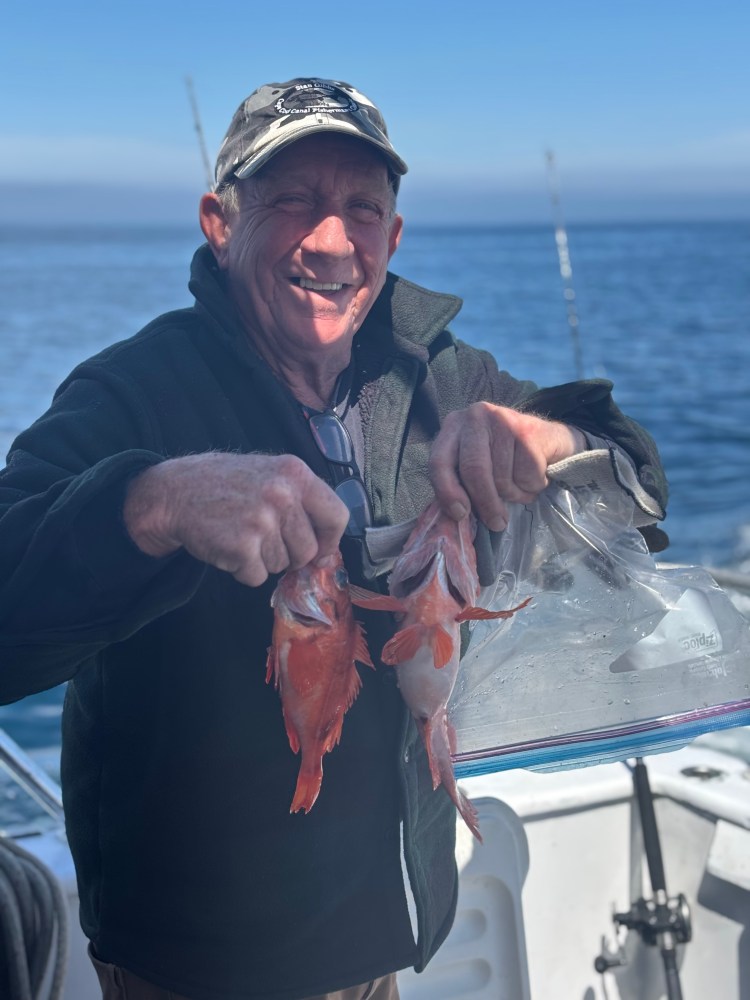 Man on a boat holding two fish and smiling.