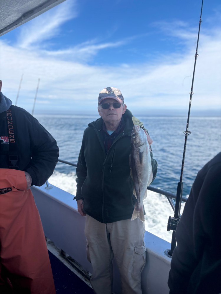Man holding a fish on a boat with ocean and blue sky background.