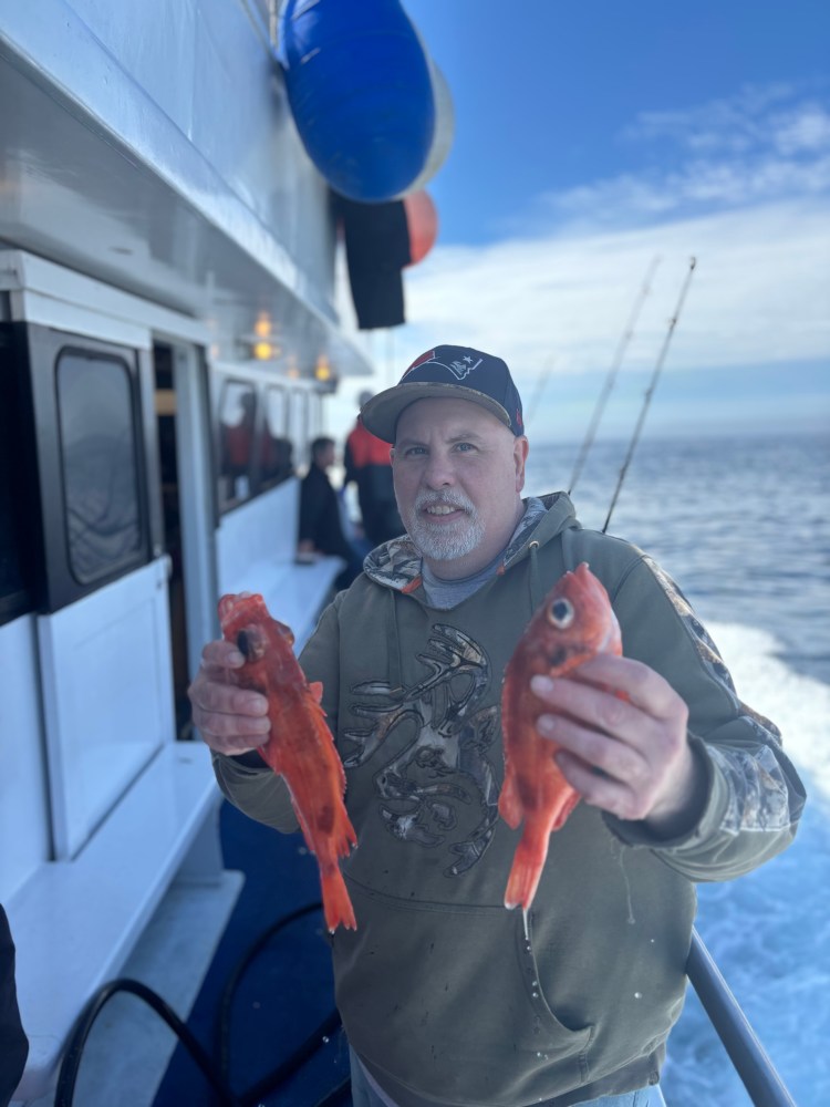 Man on boat holding two red fish with ocean in background.