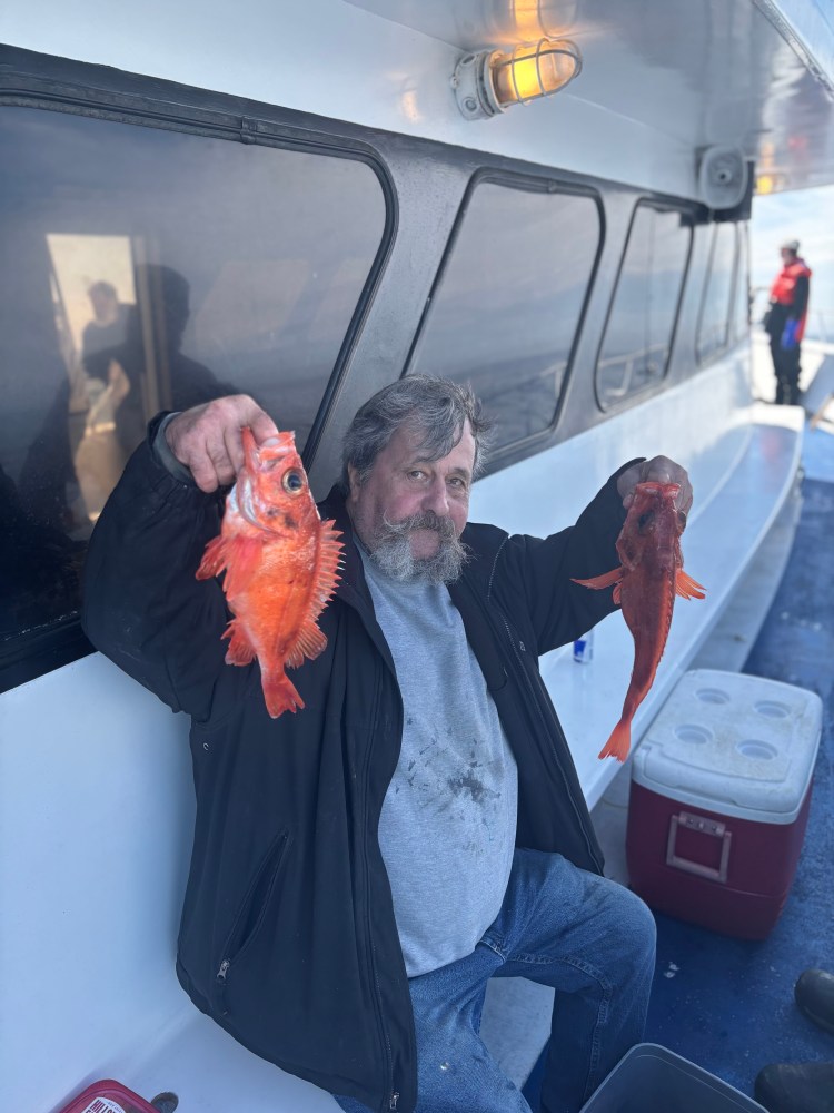 Man holding two red fish on a boat.