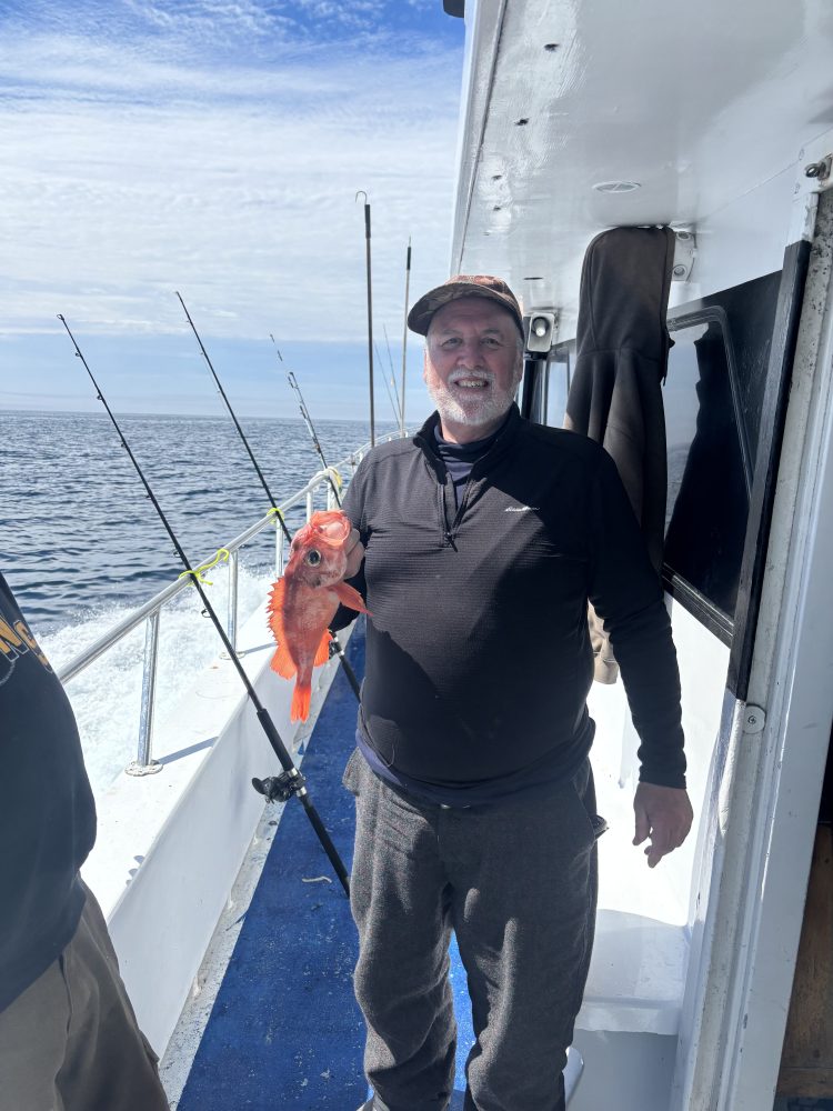 Man on boat holding a red fish, with ocean and fishing rods in background.