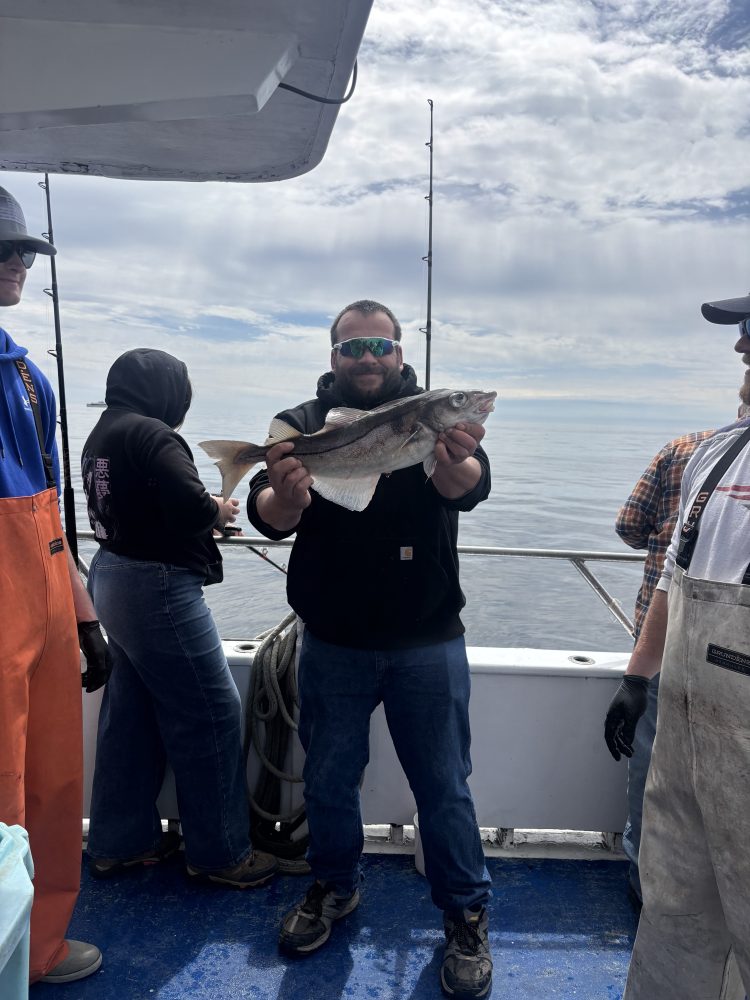 Person on a boat holding a fish, with others nearby and fishing rods visible.