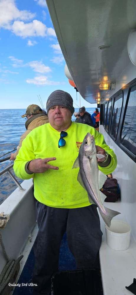 Angler in neon jacket holds fish on boat, ocean in background.