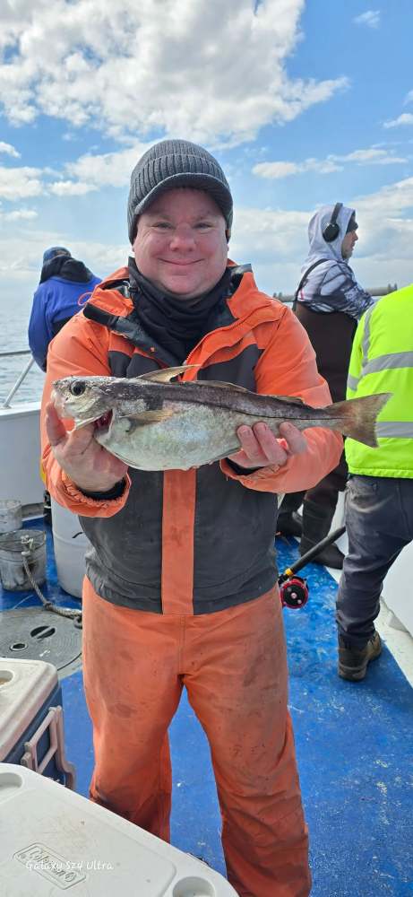 Person in orange outfit holding a fish on a boat with others on a sunny day.