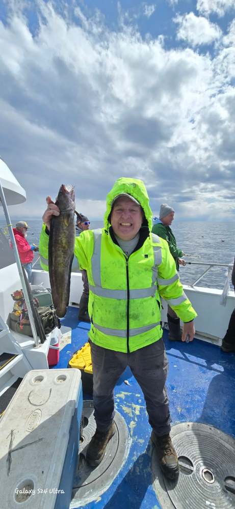 Person in a bright jacket holding a large fish on a boat at sea.
