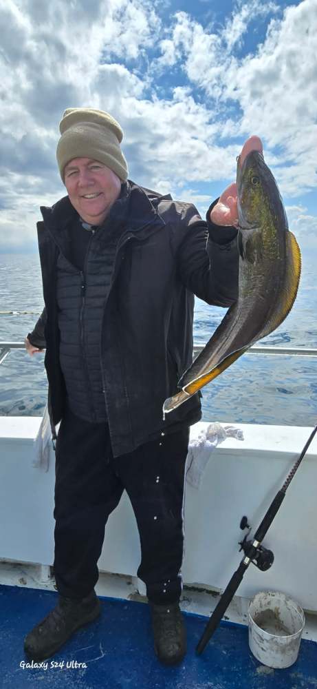 Person holding a large fish on a boat with cloudy sky background.