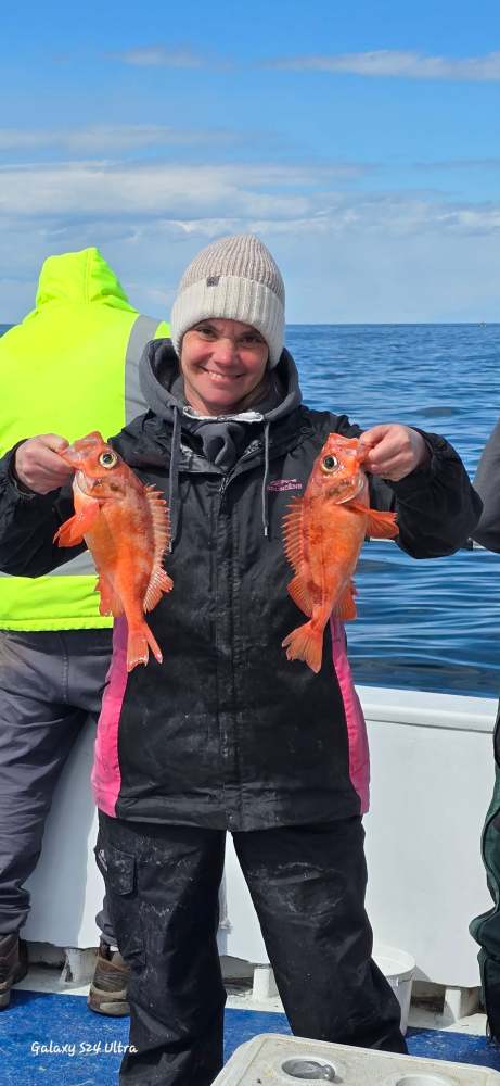 Person holding two orange fish on a boat, wearing a beanie and jacket.