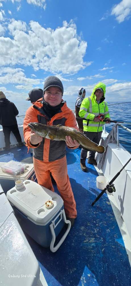 Person in orange gear holding a fish on a boat under a cloudy sky.