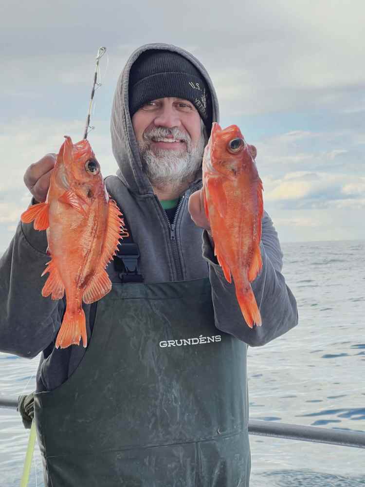 Smiling person holding two red fish on a boat.