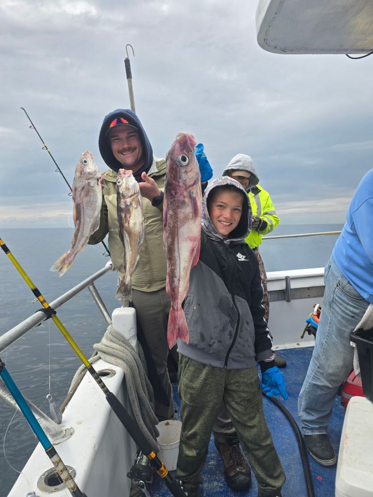 Two people on a boat holding large fish with fishing rods nearby.