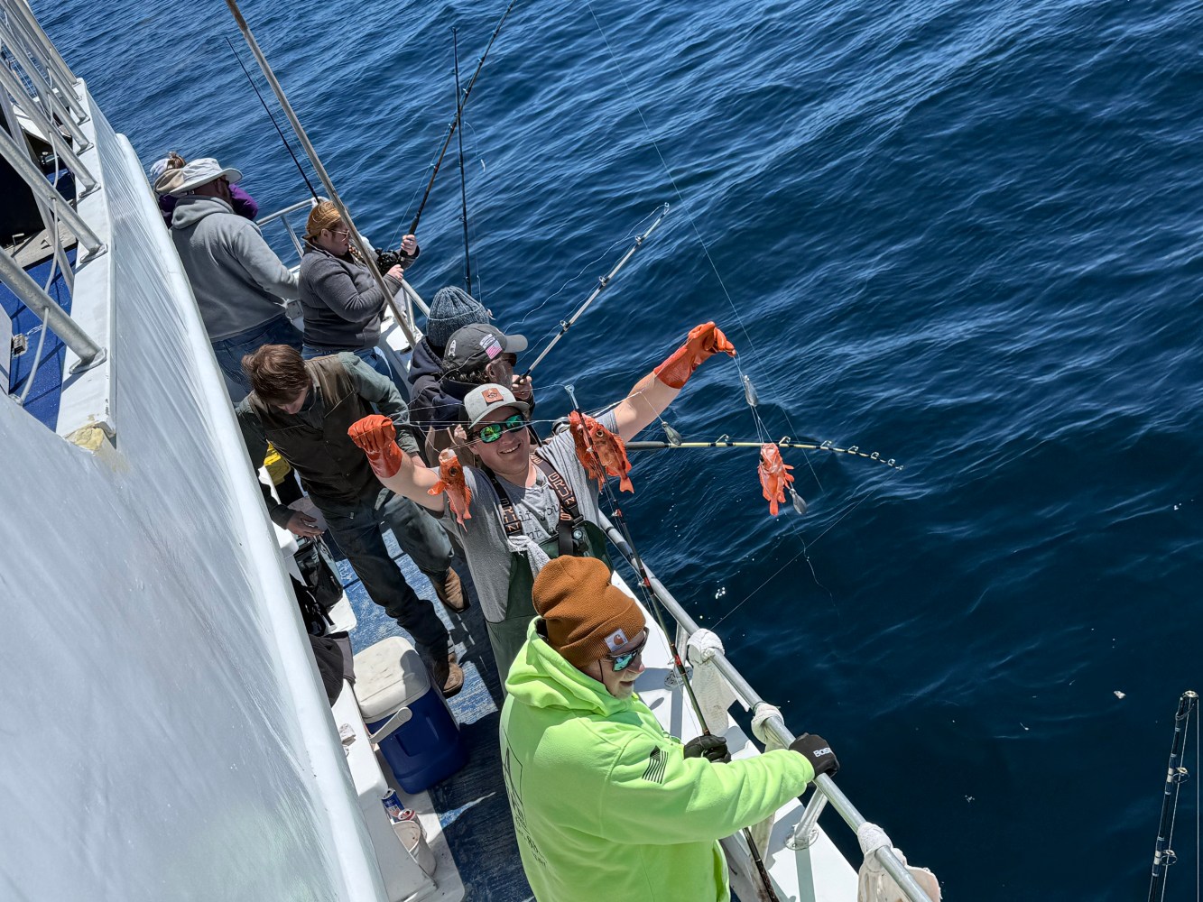 People fishing from a boat on the ocean, one person holds a caught fish.