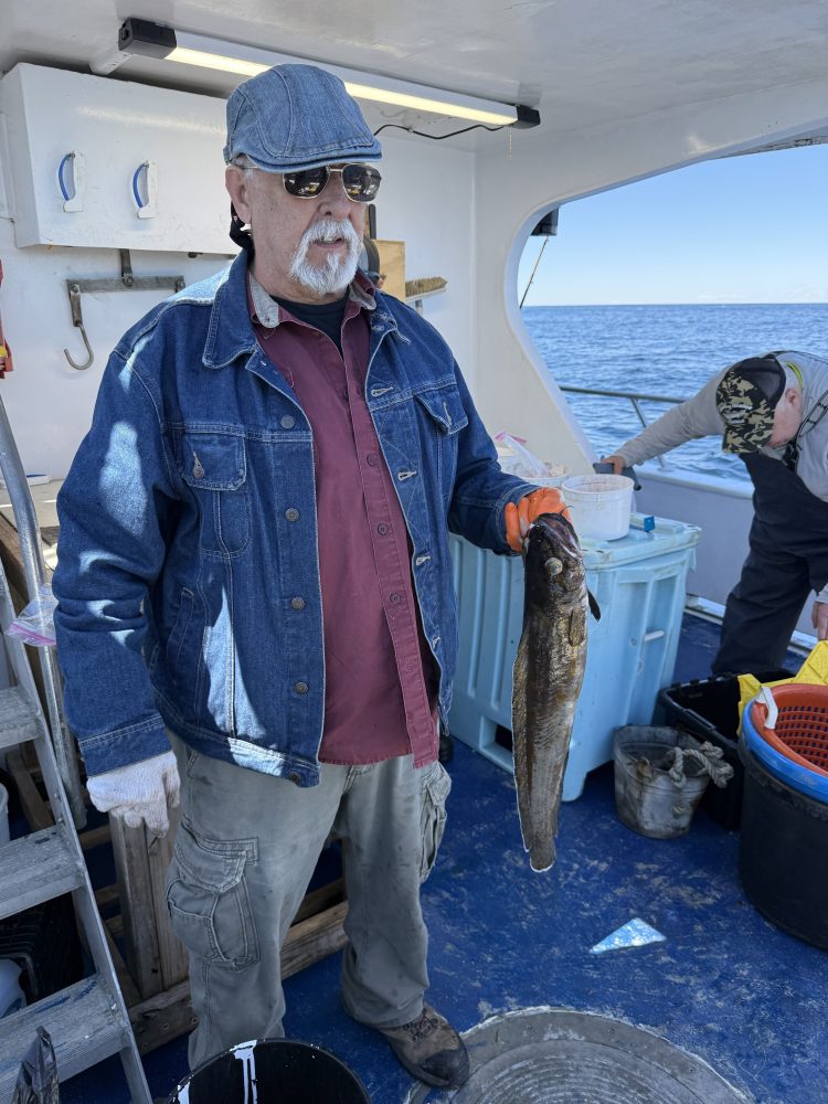 Person holding a fish on a boat wearing a denim jacket and cap.