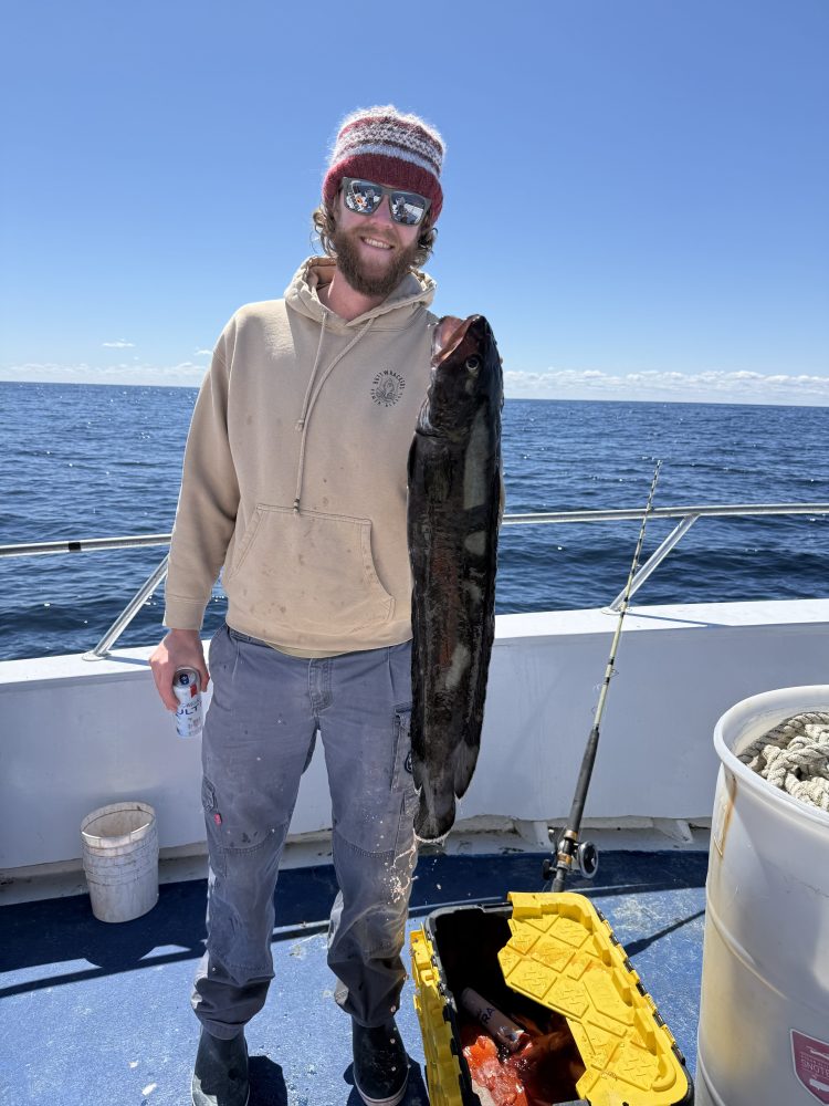 Person on boat holding a large fish next to fishing equipment.