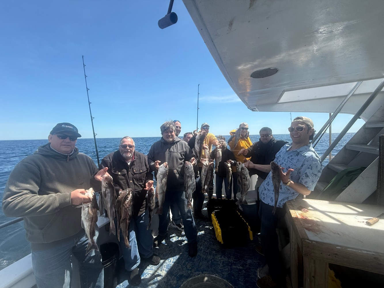 Group of people on a boat holding fish against a clear sky.