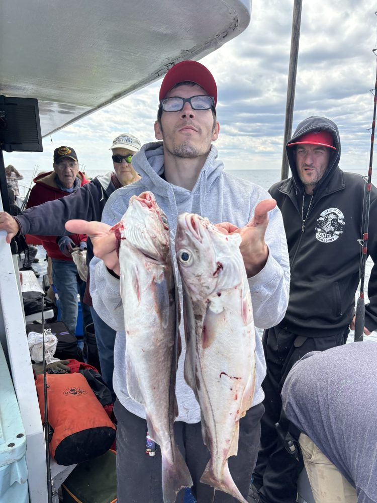 Person holding two fish on a boat with others in the background.