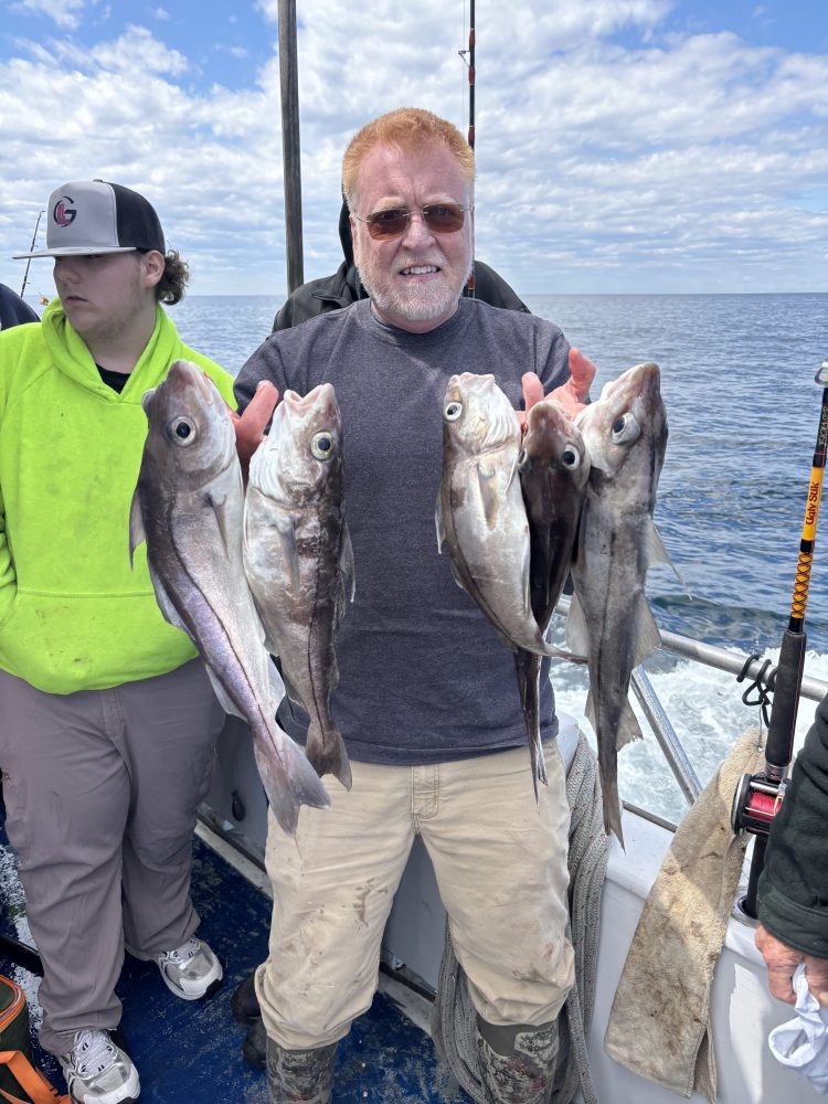 Person on a boat holding multiple fish, with ocean in the background.