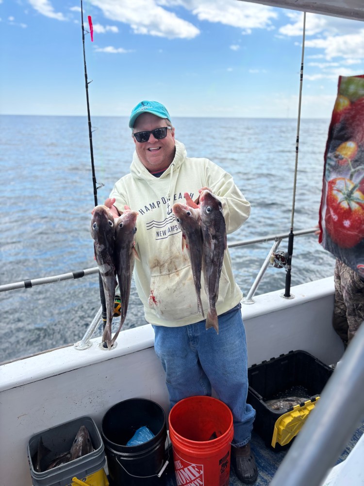 Person on boat holding two fish, smiling, with fishing rods and sea in background.