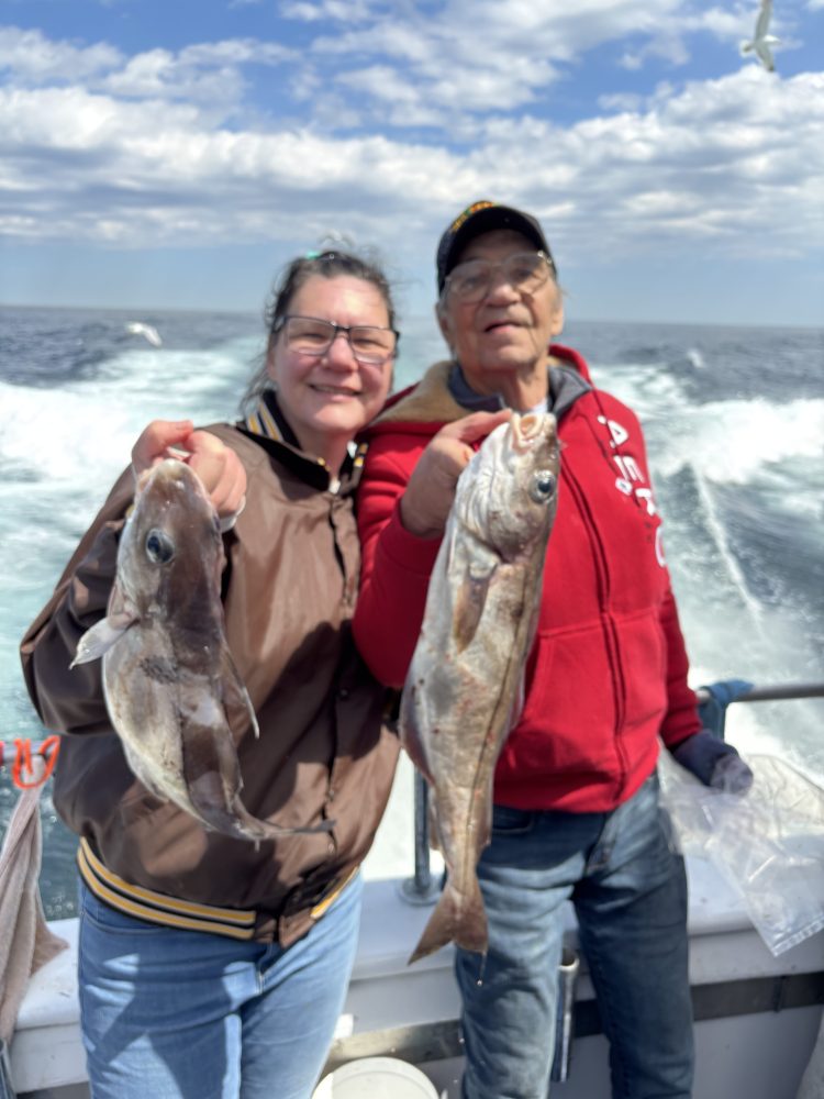 Two people holding fish on a boat with ocean in the background.