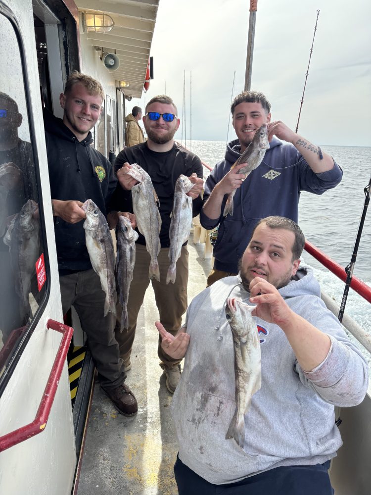 Four men on a boat holding fish, smiling at the camera.