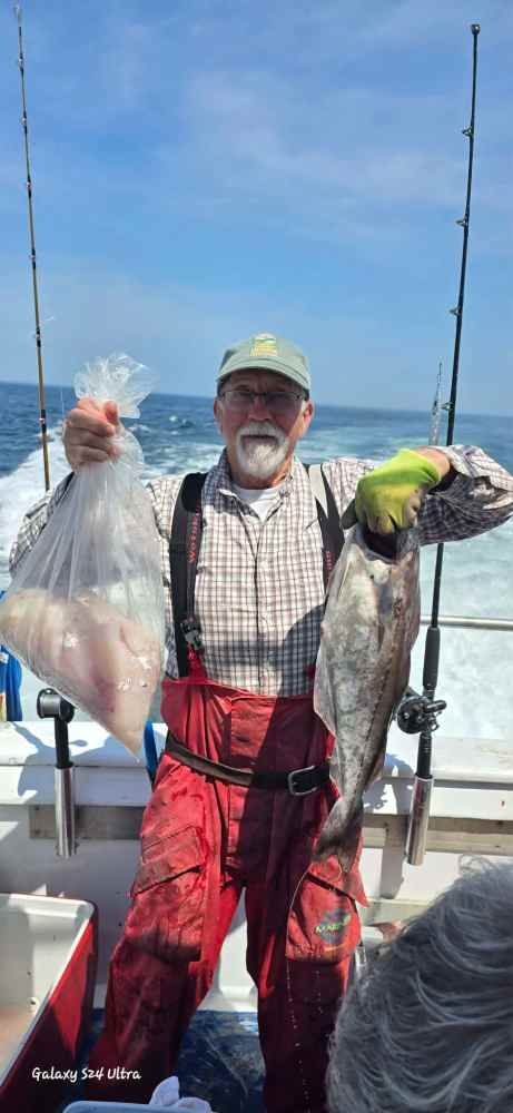 Man on boat holding a fish and a bag with more fish.
