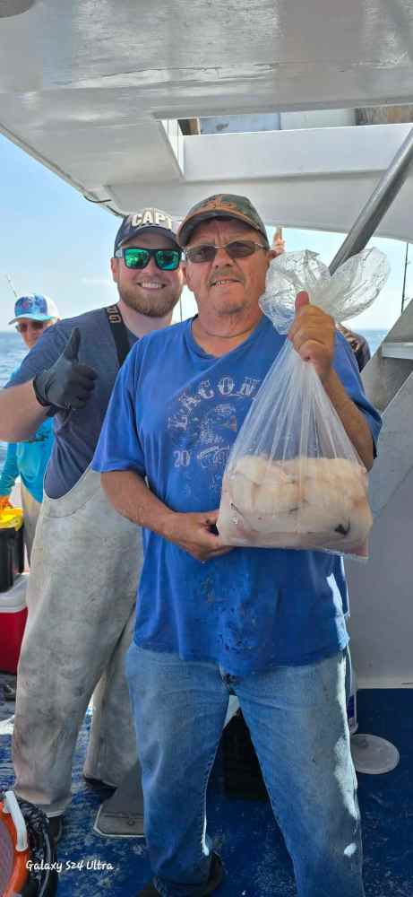 Two people on a boat, one holding a bag of fish, the other giving a thumbs up.