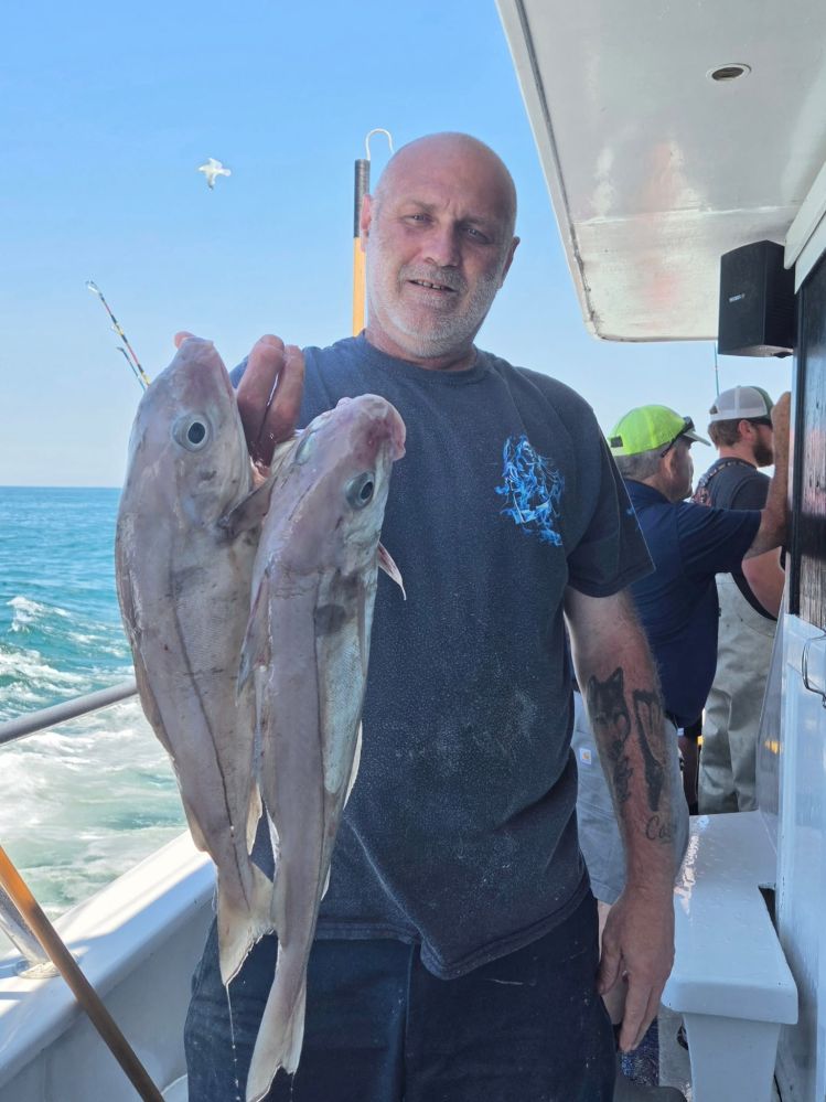 Man holding two large fish on a boat with ocean in background.