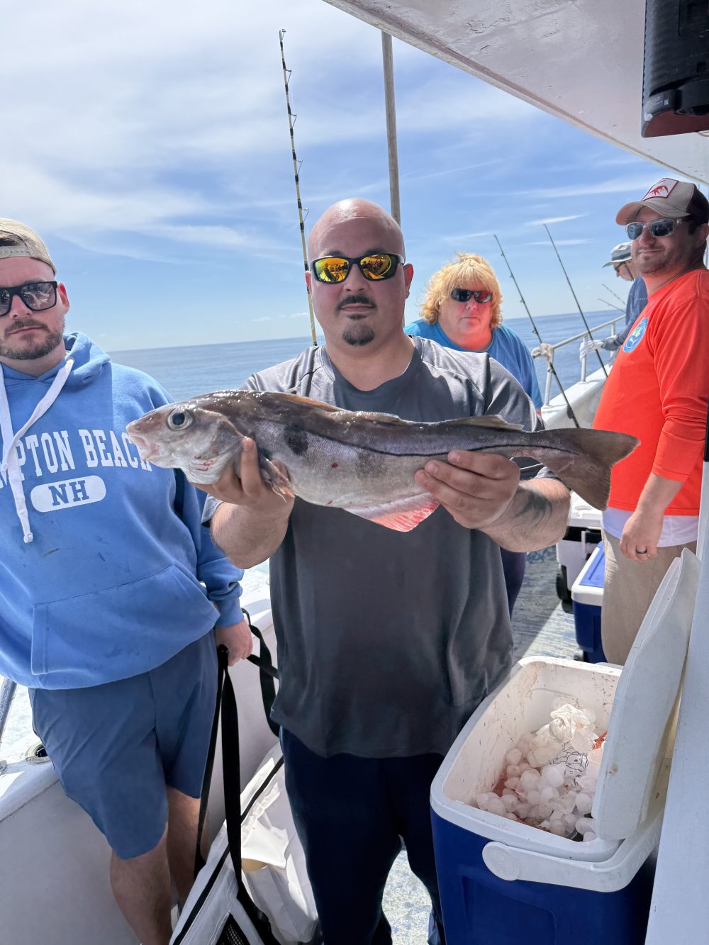 Group of people on boat, man holding a fish, cooler with ice visible.