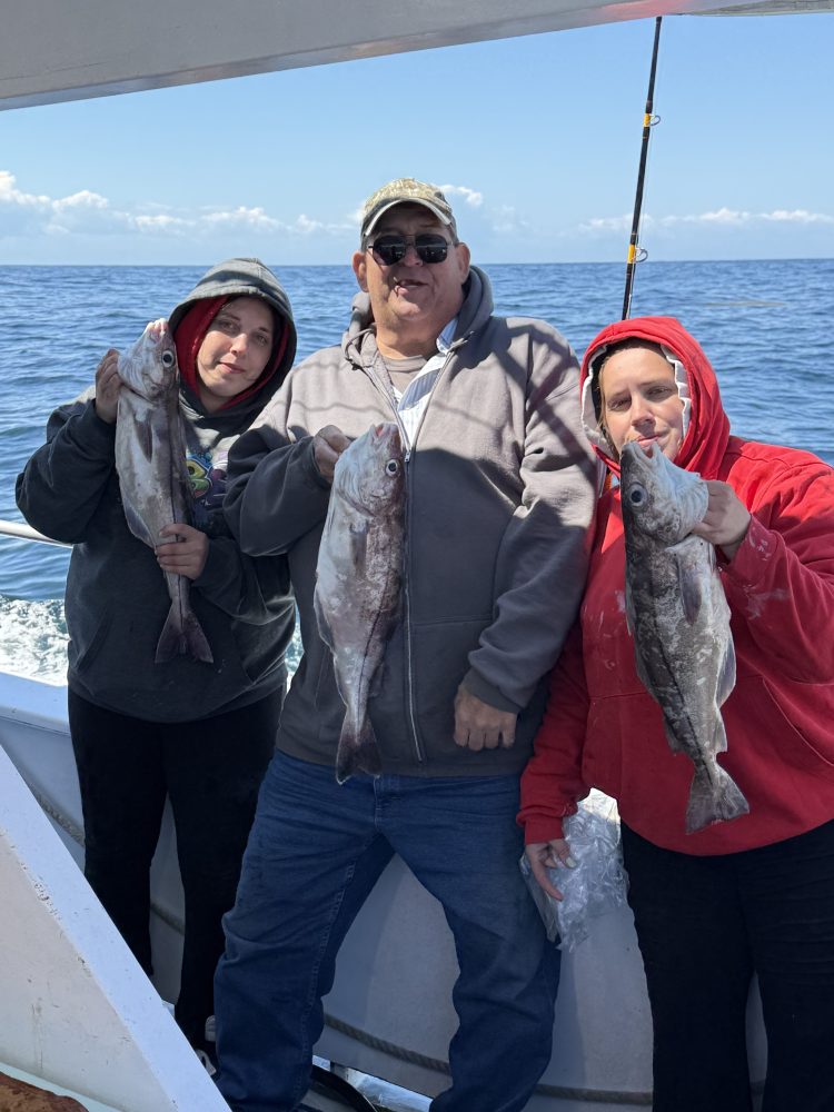 Three people on a boat holding fish, with ocean in the background.