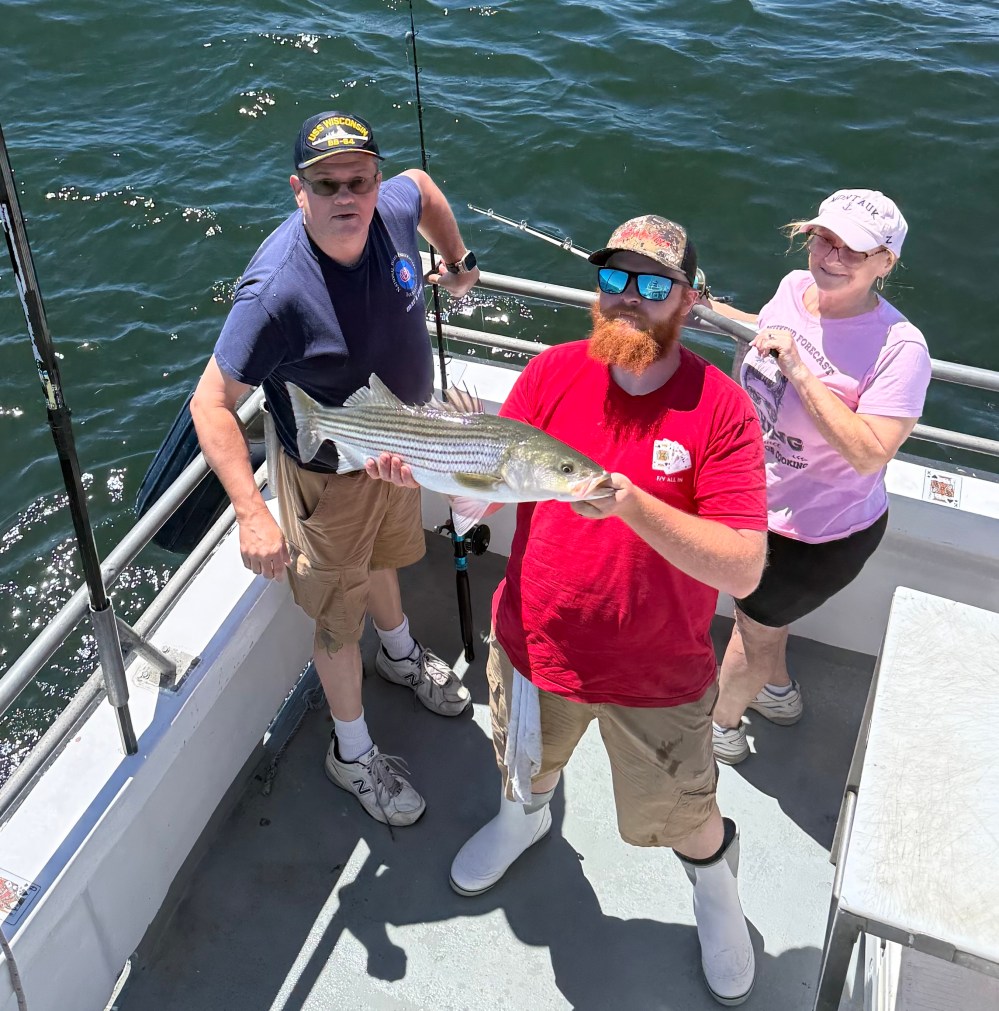 Three people on a boat holding a large fish, with water in the background.