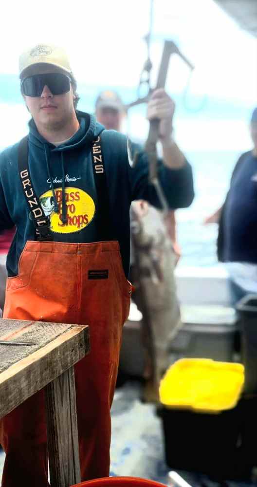 Person in orange overalls holding a fish on a boat.