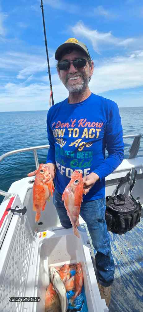 Man on boat holding two fish, wearing blue shirt and sunglasses.