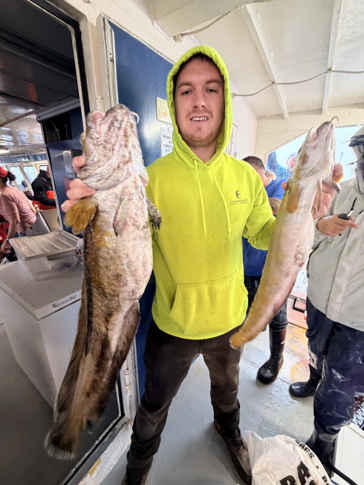 Person in a bright hoodie holding two large fish on a boat.