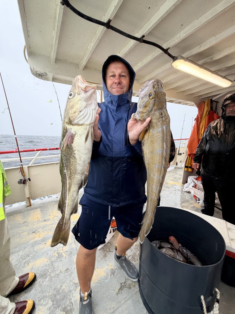Person on boat holding two large fish, smiling.